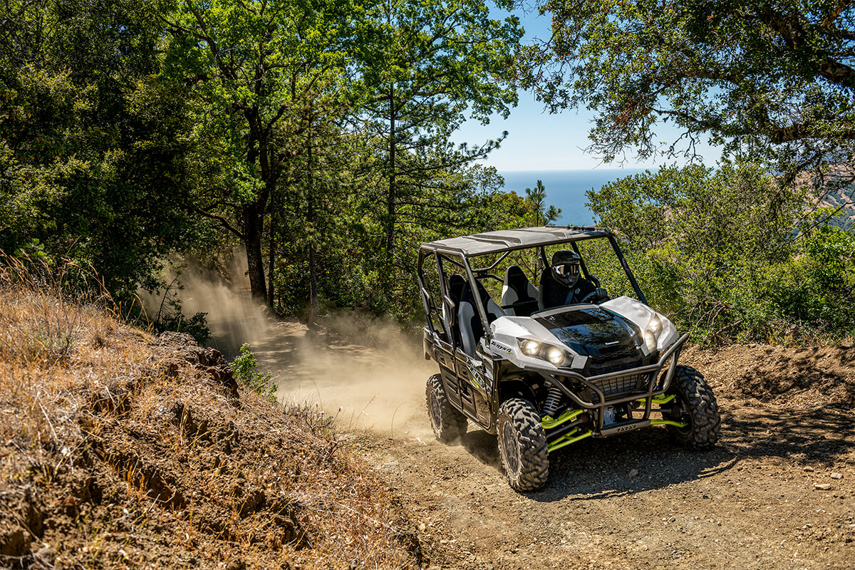 Off-road vehicle driving on a dirt trail through a forested area with a scenic background.
